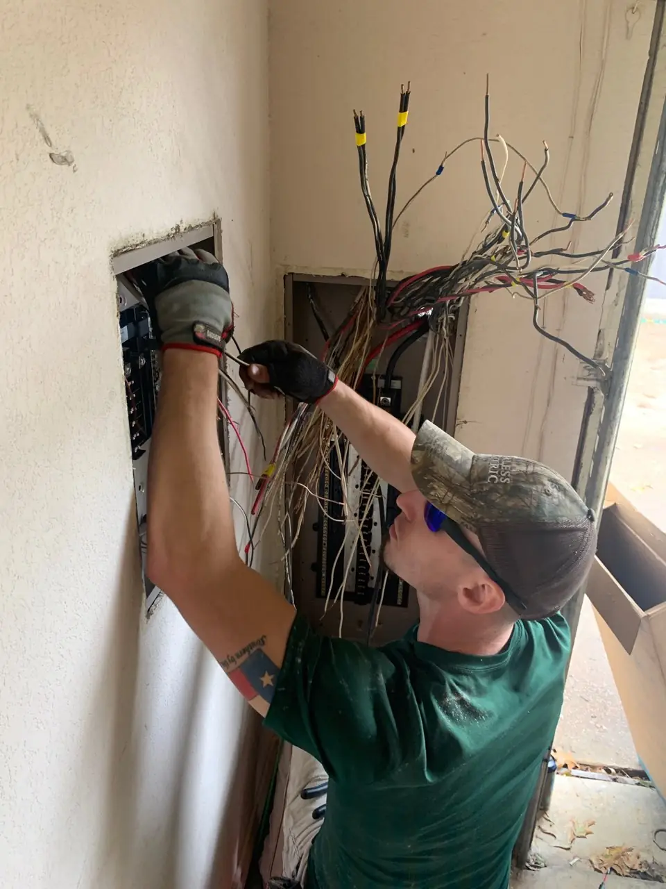 Peerless Electric technician mid rewire, reaching into an open service panel with a cut bundle of conductors
