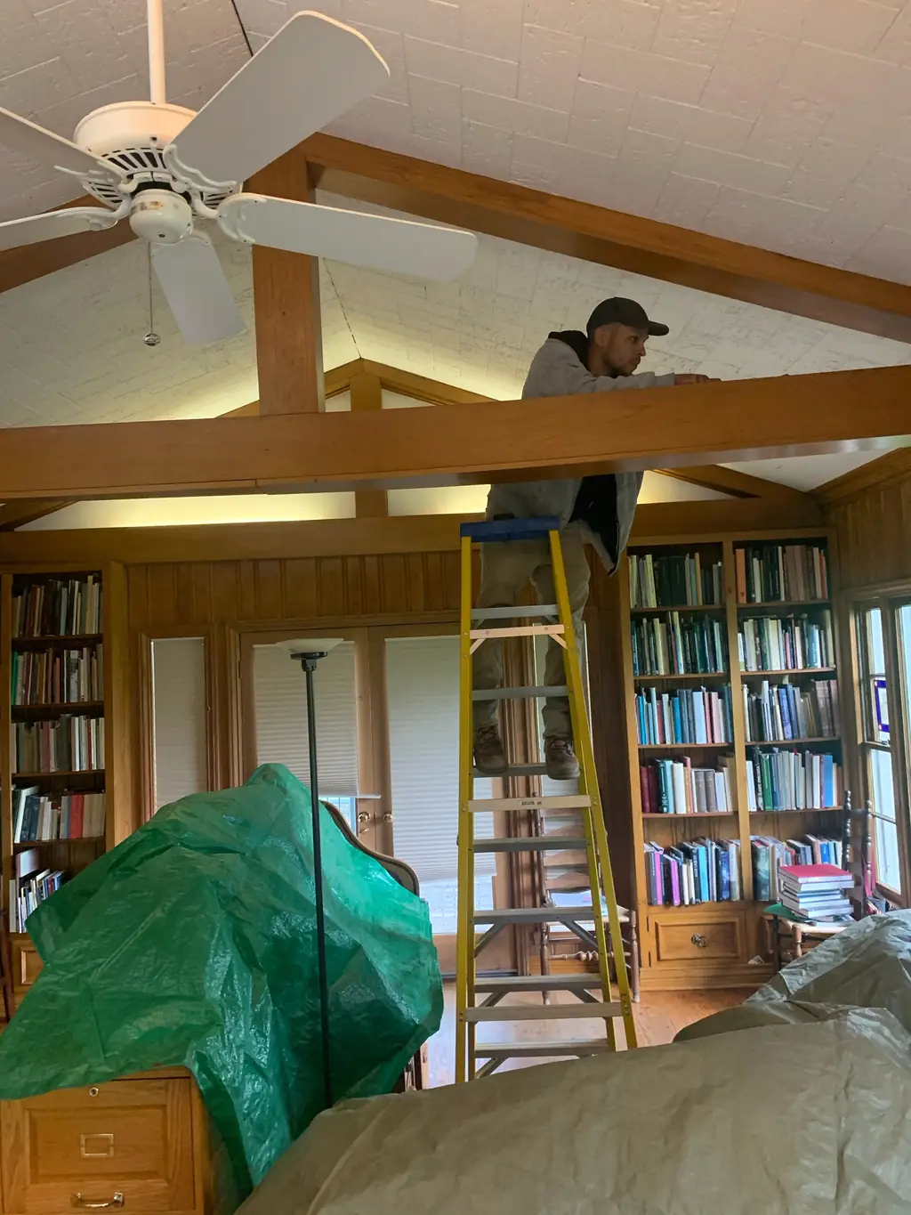 Peerless Electric technician on a ladder working ceiling wiring inside a residential room