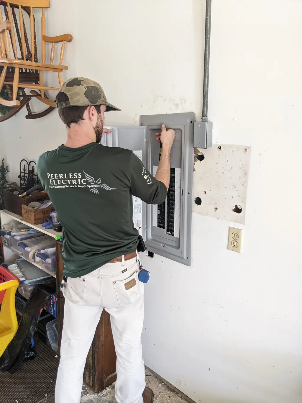 Peerless Electric technician in a branded long sleeve shirt working a garage service panel